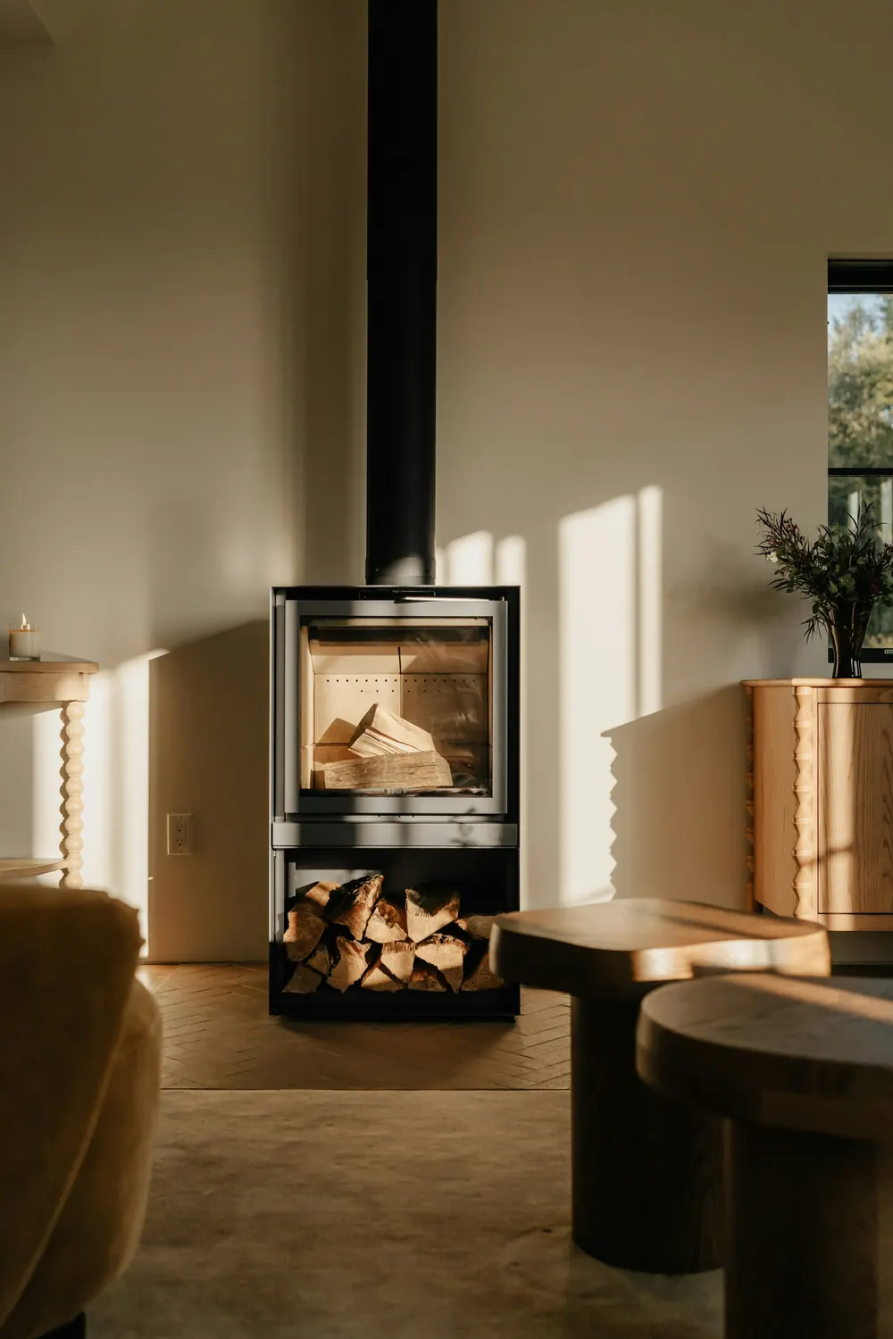 Poêle à bûches contemporain et sa réserve de bois dans un salon ensoleillé